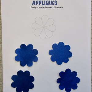 May include: A sheet of paper with the text "Creations by Melodie" and "APPLIQUÉS". Four blue flower-shaped appliqués are displayed below a drawn flower outline. The appliqués are ready to iron in place and stitch down.