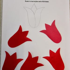 May include: Five red felt tulip appliques ready to iron and stitch down. The appliques are shaped like tulips with five petals each. The text "APPLIQUES" is written in blue on a white background. The text "Ready to iron in place and stitch down." is written in black on a white background.