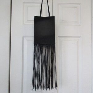 May include: A black leather tote bag with a long fringe detail hanging from a white hook.