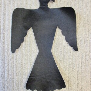 May include: A black silhouette of a bird with outstretched wings. The bird has a detailed head and beak, with a stylized body and tail. The cutout is likely made of felt or a similar material, and is placed against a textured, light-colored background.