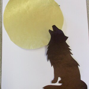 May include: A dark brown paper cutout of a howling wolf positioned next to a large, circular, pale yellow paper moon. The text Wolf 5.75 inches is written in the top right corner of the white paper background.