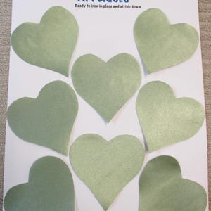 May include: A sheet of appliqués featuring seven sage green heart shapes. The text "APPLIQUÉS" is printed in blue, with the words "Creations by Melodie" above and "Ready to iron in place and stitch down" below.