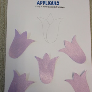 May include: Five purple felt tulip appliques ready to iron and stitch down. The appliques are on a white sheet of paper with the words "Appliques" and "Ready to iron in place and stitch down." printed in blue.