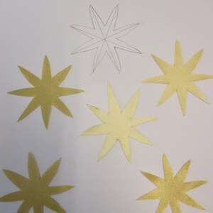 May include: Gold star appliqués on white paper, with the text "APPLIQUÉS" and "Ready to iron in place and stitch down." The appliqués are approximately 2.75 inches in size. One star is a pencil outline.