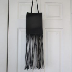 May include: A black leather tote bag with a long fringe detail hanging from a white hook.
