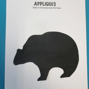 May include: Black felt applique of a bear silhouette. The text "APPLIQUES" is printed above the bear. The text "Ready to iron in place and stitch down." is printed below the bear.