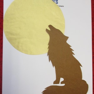 May include: A brown paper silhouette of a wolf howling at a large yellow paper moon.