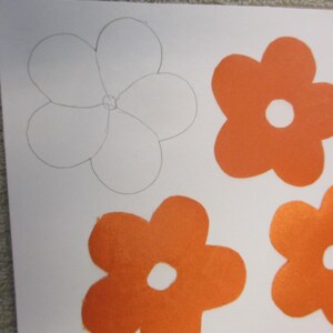 May include: A white paper with a pencil drawing of a flower and four orange felt flowers.