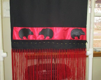Peut inclure: Suspension murale textile noire avec une bande de satin rouge ornée de trois silhouettes d'ours. Le bord inférieur est orné de longues franges rouges. De petites perles dorées sont cousues le long du bord supérieur de la bande de satin rouge.