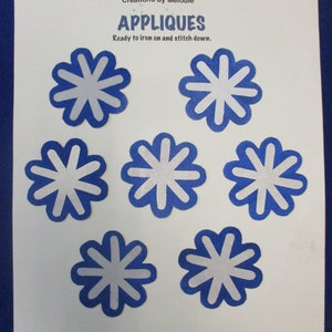 May include: Six blue felt appliques with white starburst designs. The appliques are ready to iron on and stitch down. The text "APPLIQUES" is printed on the white paper background.