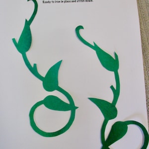 May include: Two green vine-shaped fabric appliqués on a white background. The text reads: Creations by Melodie, APPLIQUES, Ready to iron in place and stitch down. A handwritten note indicates 8.25 inches tall for these iron-on vine pieces.