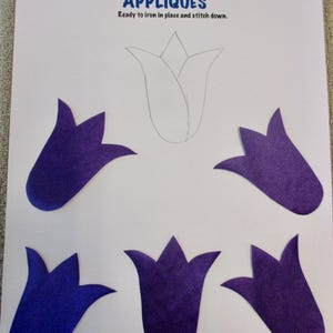 May include: Five purple felt tulip shapes ready to be ironed and stitched onto a craft project. The title "Appliqués" and the text "Ready to iron in place and stitch down." are printed on the white paper.