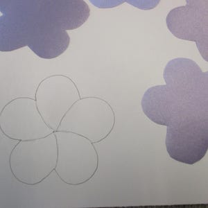 May include: A white sheet of paper with a pencil drawing of a flower with five petals. There are four purple paper flowers on the sheet of paper.