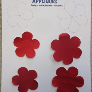 May include: A sheet with red flower appliqués and outlines for cutting. The text "APPLIQUÉS" is in blue. The appliqués are approximately 2.5 and 3 inches in diameter. The text "Ready to iron in place and stitch down" is also present.