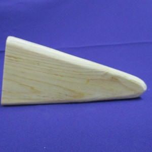 May include: A light wood wedge shaped block. The block is smooth and has a natural wood grain.