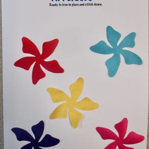 May include: A sheet of paper with five colorful flower appliqués in red, blue, yellow, purple, and pink. Text at the top reads "Creations by Melodie" and "APPLIQUÉS, Ready to iron in place and stitch down."