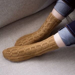 May include: A pair of brown knitted socks with a cable knit pattern. The socks are worn on a person's feet.