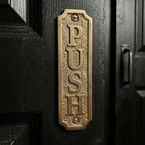 May include: A white ceramic mug with a black handle and the text "But First, Coffee" in a black, bold font. The mug is sitting on a wooden surface. The mug is approximately 4 inches tall.