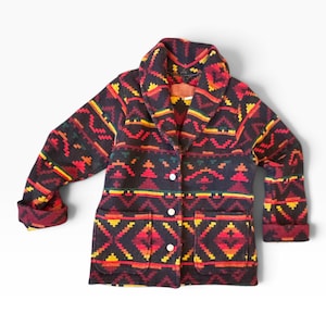 Puede incluir: Una chaqueta de manga larga con cuello de chal, con un color base oscuro y un patrón geométrico en tonos rojo, naranja, amarillo y verde. La chaqueta incluye tres botones blancos en la parte delantera y dos grandes bolsillos de parche.