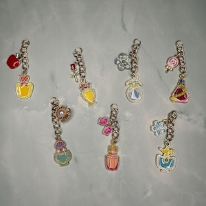 Peut inclure: Huit porte-clés en forme de flacon de parfum. Chaque porte-clés présente un design différent, notamment une pomme rouge, une rose, une fleur et une sucette. Les porte-clés sont de différentes couleurs, dont le jaune, le rose et le bleu.