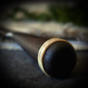May include: Close-up of a dark brown wooden object with a rounded, black end. A light-colored ring encircles the end, creating a contrast. The object has a smooth, polished appearance, suggesting a handcrafted item.