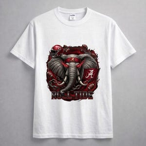 Pode incluir: Camiseta branca com um gráfico de um elefante com um capacete de futebol e o texto "Roll Tide". O elefante tem uma faixa vermelha na cabeça e é cercado por bolas de futebol e correntes. A letra "A" está na bandeira.