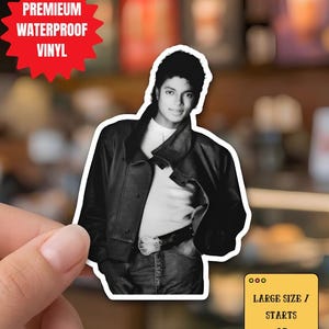 Könnte beinhalten: Ein schwarz-weißer Aufkleber mit Michael Jackson in Lederjacke und Jeans. Der Aufkleber trägt den Text „PREMIUM WATERPROOF VINYL“ und „LARGE SIZE / STARTS AT: 7.6x10.2 cm“. Der Hintergrund ist unscharf.