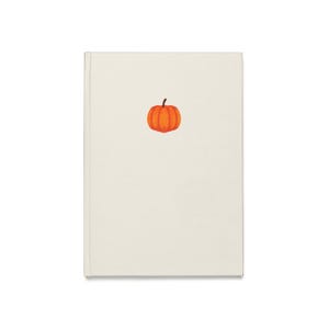Pode incluir: Um caderno retangular com uma capa lisa em tom de branco sujo. Centralizada na capa frontal, encontra-se uma pequena ilustração simples de uma abóbora laranja brilhante com um caule castanho escuro e sulcos verticais.