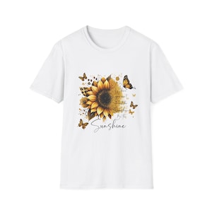 Puede incluir: Camiseta blanca con un diseño de girasol, mariposas y el texto "When you can't find the sunshine, be the sunshine." El diseño utiliza colores amarillo, naranja y marrón.