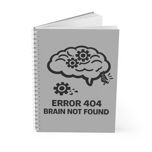 Puede incluir: Un cuaderno gris con espiral con una ilustración negra de un cerebro con engranajes y el texto "ERROR 404 BRAIN NOT FOUND". El cuaderno está abierto, revelando páginas blancas.