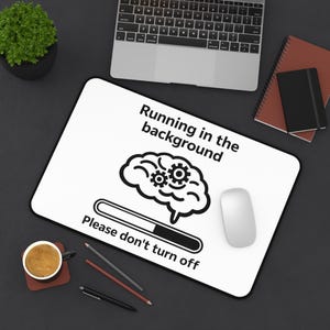 Może przedstawiać: Biała prostokątna podkładka pod mysz z czarną obwódką. Zawiera tekst "Running in the background" i "Please don't turn off", a także grafikę mózgu z zębatkami i paskiem ładowania. Widoczna jest również biała mysz i laptop.