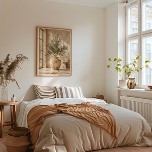 Könnte beinhalten: Ein Schlafzimmer mit einem Bett, das eine beigefarbene Bettdecke und eine rostfarbene Tagesdecke sowie zwei gestreifte Kissen hat, einem Holztisch mit einer Glasvase mit Trockenpflanzen, einem gerahmten Wandbild eines Olivenbaums und einem Fenster.