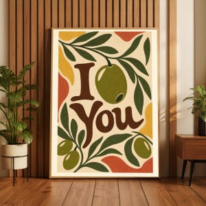 以下が含まれることがあります： ダークブラウンのスタイリッシュな文字で「I You」と書かれた、長方形の額入りウォールアートプリント。クリーム色の背景に、抽象的な黄色とオレンジ色の形、そして葉のついた緑色のオリーブのイラストが描かれています。