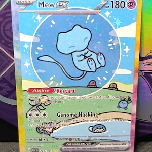 Op de afbeelding: Een Mew ex ruilkaart met een lichtblauw Mew-personage in een cirkelvormig kader tegen een hemelsblauwe achtergrond. Het onderste gedeelte toont een groen veld met kleine Pokémon-illustraties, de tekst Restart en Genome Hacking, met 180 HP.