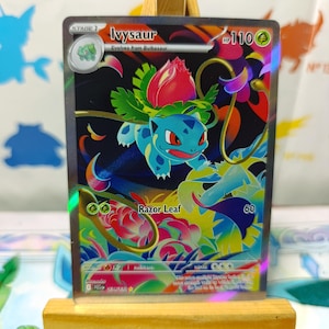Könnte beinhalten: Eine holografische Ivysaur-Sammelkarte mit einem blauen Wesen, das eine rosa Blumenknospe auf dem Rücken trägt. Die Karte zeigt den Namen Ivysaur, 110 KP und die Angriffsattacke Rasierblatt. Das Kunstwerk ist lebendig mit bunten, wirbelnden Mustern.