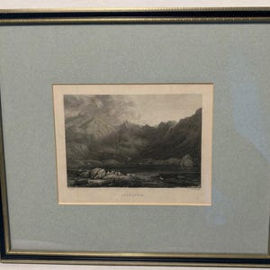 May include: Framed black and white landscape print depicting a mountain range and lake. The print is set within a light blue mount and a black and gold frame. The print is labelled "Loch Leven".