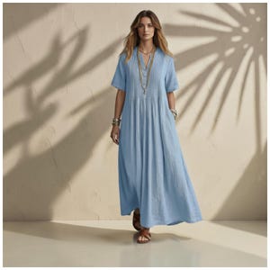 Peut inclure: Une robe longue bleu clair à manches courtes, dotée d'un col en V et de plis verticaux sur le corsage. La robe présente une jupe ample et fluide qui arrive aux chevilles. Elle est portée avec des sandales en cuir marron et un collier doré.
