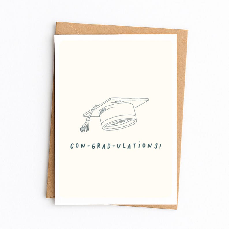 Op de afbeelding: Een cr&egrave;mekleurige wenskaart met een eenvoudige zwarte lijntekening van een afstudeerhoed met een kwastje. Onder de illustratie staat de tekst CON-GRAD-ULATIONS! in het zwart gedrukt. De kaart zit in een bruine envelop van kraftpapier.