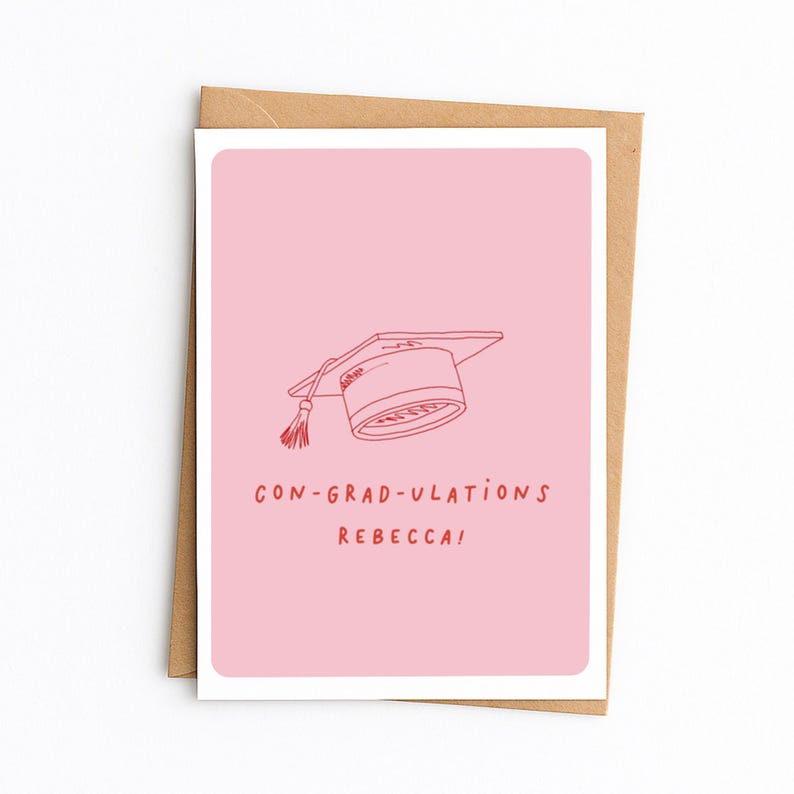 Op de afbeelding: Een rechthoekige wenskaart met een lichtroze achtergrond met een rode lijntekening van een afstudeerhoed met een kwastje. Onder de illustratie staat de tekst CON-GRAD-ULATIONS REBECCA! in rode hoofdletters.
