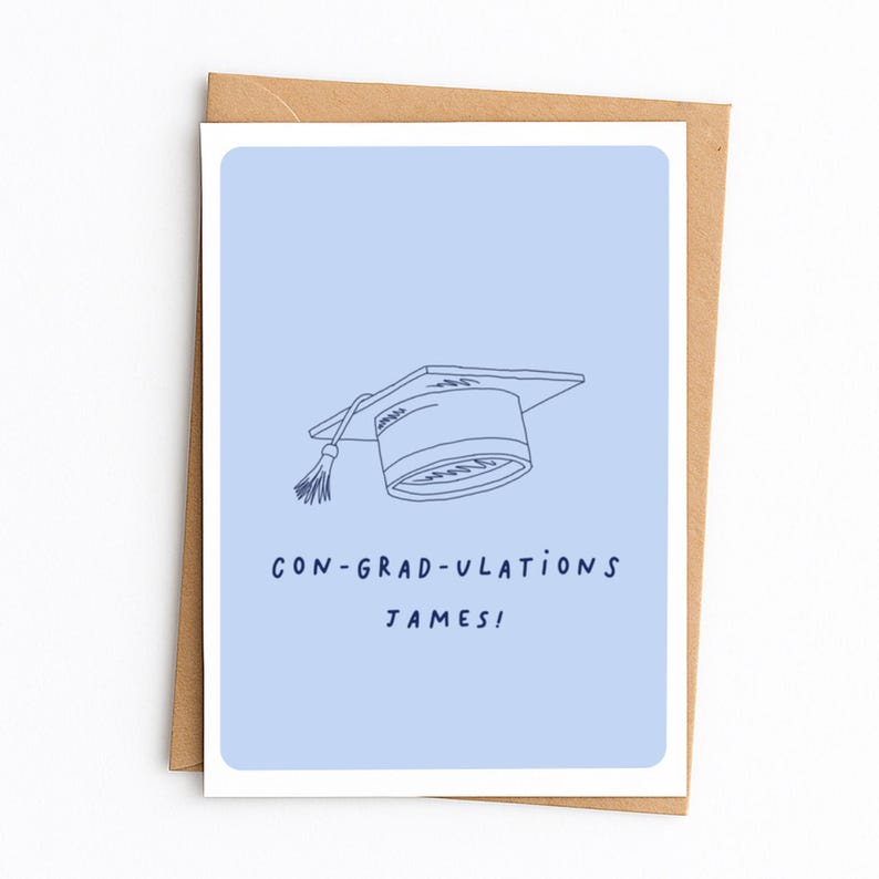 Op de afbeelding: Een lichtblauwe wenskaart met een donkerblauwe lijntekening van een afstudeerhoed met een kwastje. Onder de illustratie staat de tekst CON-GRAD-ULATIONS JAMES! in donkerblauwe hoofdletters. De kaart ligt op een bruine envelop.