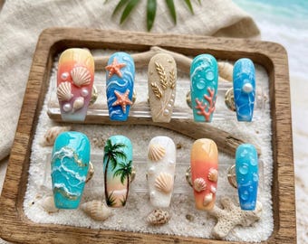 Puede incluir: Una colección de diez uñas artificiales con varios diseños con temática de playa. Cada uña presenta diferentes colores y decoraciones, incluyendo conchas marinas, estrellas de mar, coral y palmeras. Las uñas se exhiben en una bandeja de madera con arena y conchas.