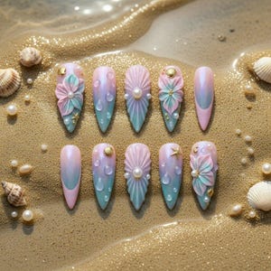 May include: A set of ten long, pointed artificial nails with a mermaid theme. The nails feature a gradient of pink, blue, and purple, with seashell, pearl, and floral embellishments. Some nails have 3D flower designs, while others have pearl accents.