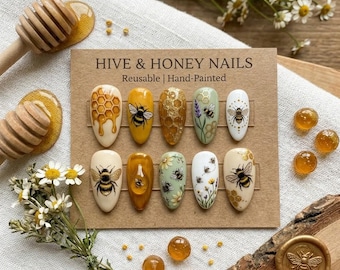Puede incluir: Un conjunto de diez diseños de arte de uñas reutilizables y pintados a mano con un tema de abeja y panal. Las uñas presentan varios diseños, incluyendo abejas, panales y acentos florales. La tarjeta dice "HIVE & HONEY NAILS".