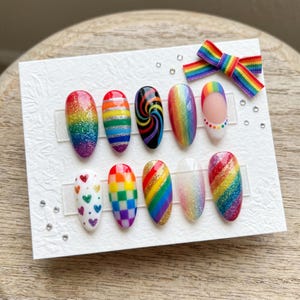 Pode incluir: Um conjunto de dez unhas postiças com vários desenhos de arco-íris, incluindo glitter, listras e espirais. Uma fita de arco-íris também está incluída, tudo em um cartão branco.