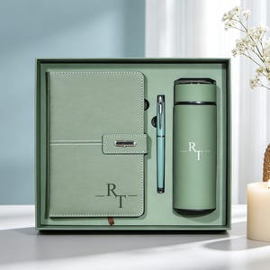 May include: A sage green gift set containing a notebook with a silver clasp, a matching ballpoint pen, and a cylindrical insulated bottle. Both the notebook and the bottle feature the monogram RT in a serif font. The items are arranged in a box.