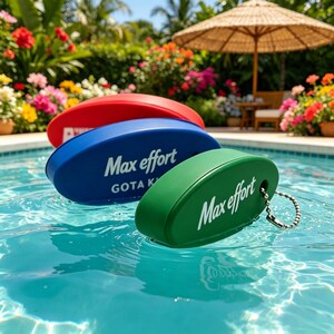 May include: Three oval-shaped floating keychains in red, blue, and green, each featuring the white text Max effort. The blue and green keychains include a silver metal ball chain. These items are partially submerged in clear blue swimming pool water.