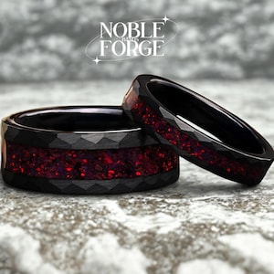 Könnte beinhalten: Zwei schwarze Ringe mit facettiertem Design und roter, strukturierter Einlage. Die Ringe sind vor einem neutralen Hintergrund platziert. Die Ringe tragen den Text "NOBLE FORGE" in einer stilisierten Schriftart.