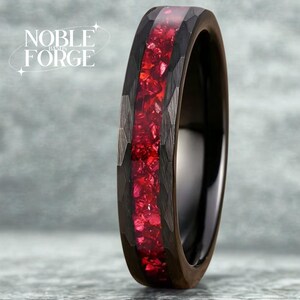 Könnte beinhalten: Ein schwarzer Ring mit einem gehämmerten, dunkelgrauen Außenband und einem leuchtend roten Mittelteil. Der Ring hat eine glänzende Oberfläche. Der Text "NOBLE FORGE" ist sichtbar.