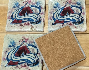 May include: Set of four square coasters with a white background and a red, white, and blue hockey team logo. The coasters have a cork backing.