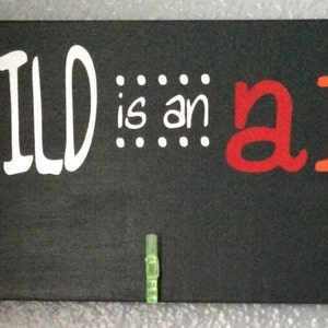 May include: Black chalkboard sign with the quote "EVERY CHILD is an artist - Pablo Picasso -" in white text. The word "artist" is written in rainbow colors. There are five colorful clothespins attached to the sign.